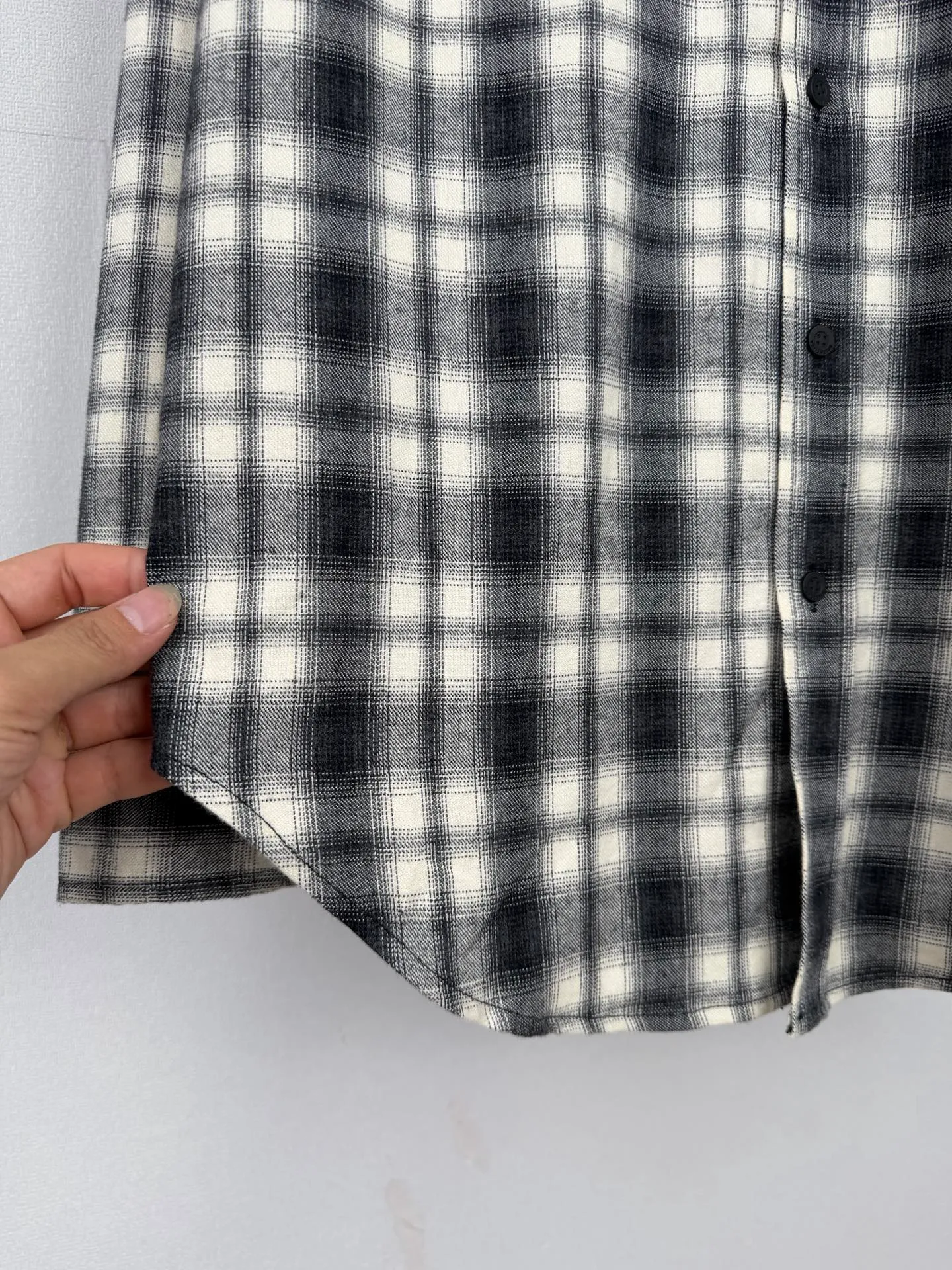 BALENCIAGA/balenciaga Black White plaid pocket embroidered logo shirt jacket The technical difficulties of this plaid shirt focus on fabric finishing, plaid matching and component sewing details. The fabric has been sanded and distressed to create a fine velvet feel on the surface, changing the original luster of the fabric and making the Black and White plaid colors transition softly. At the same time, the drape properties of the fabric itself are retained, taking into account the looseness of the upper body and the silhouette of the body, without appearing soft and shapeless. The biggest test of plaid garments comes from the alignment of the pieces. The front and rear body, large and small sleeves, and chest pockets are all independent pieces. In the cutting stage, the horizontal and vertical axes of the plaid need to be aligned, and the external chest bag is cut separately. The plaid on the bag surface needs to form a visual coordination with the main body of the garment. Cutting and typesetting will produce additional fabric loss, and there are high requirements for the cutting accuracy of the cutting bed typesetting and workers. The collar adopts a double-layer combined structure, and the collar surface and collar seat are double-stitched with even and regular stitching spacing to ensure the lapel's long-lasting shape and resistance to warping and deformation after repeated bending. The placket is sewn with regular topstitching and paired with Black matte buttons. The button points need to be aligned with the checkered lines to avoid damaging the overall visual order. The splicing of the cuffs also takes into account the grain direction, and the overlocking process reinforces the seams to improve the durability of the garment. After the entire garment is sewn, it also undergoes a garment washing process to further strengthen the Retro texture of the fabric, unify the tone and texture of the entire garment, weaken the harshness of industrial production, and finally present a relaxed Retro garment effect. Size: 46 48 50 52
